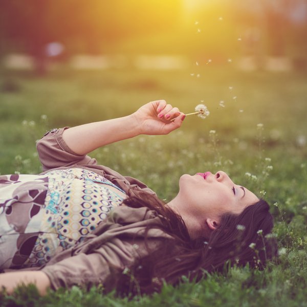 Frau liegend auf Wiese mit Pusteblume